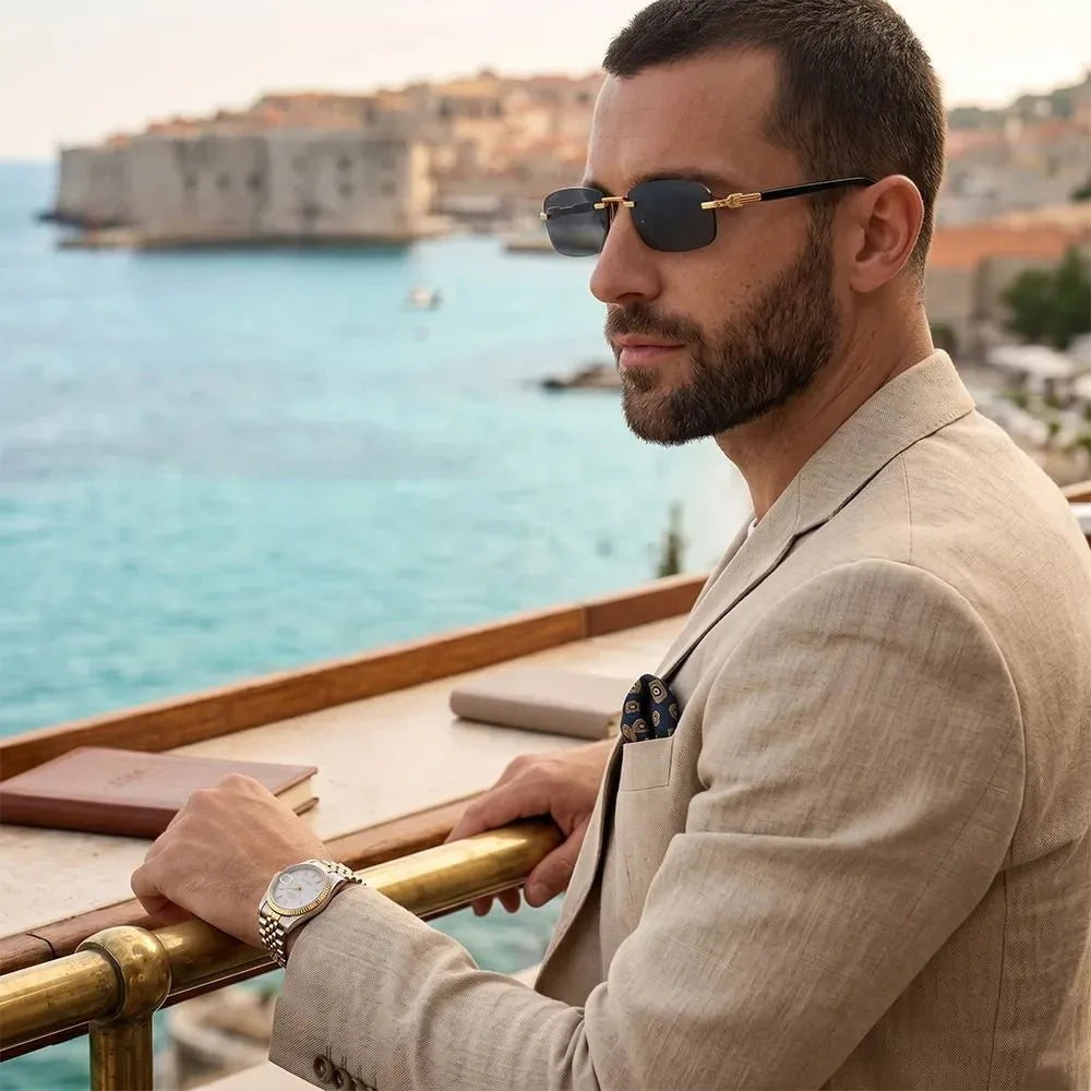 Man in a beige linen suit wearing luxury square sunglasses overlooking a coastal city.