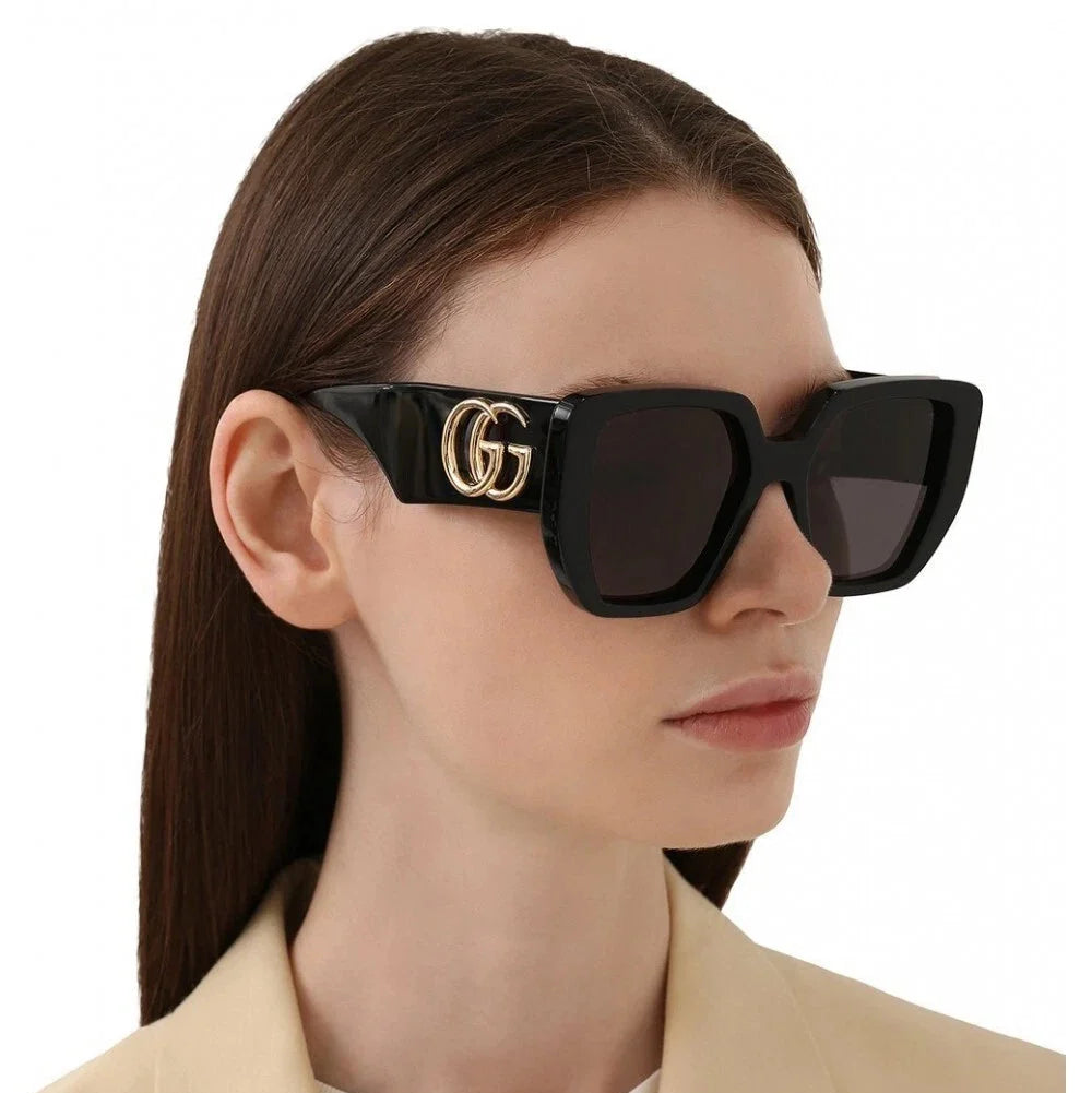 Woman wearing oversized black luxury sunglasses with a gold G logo on the temple.