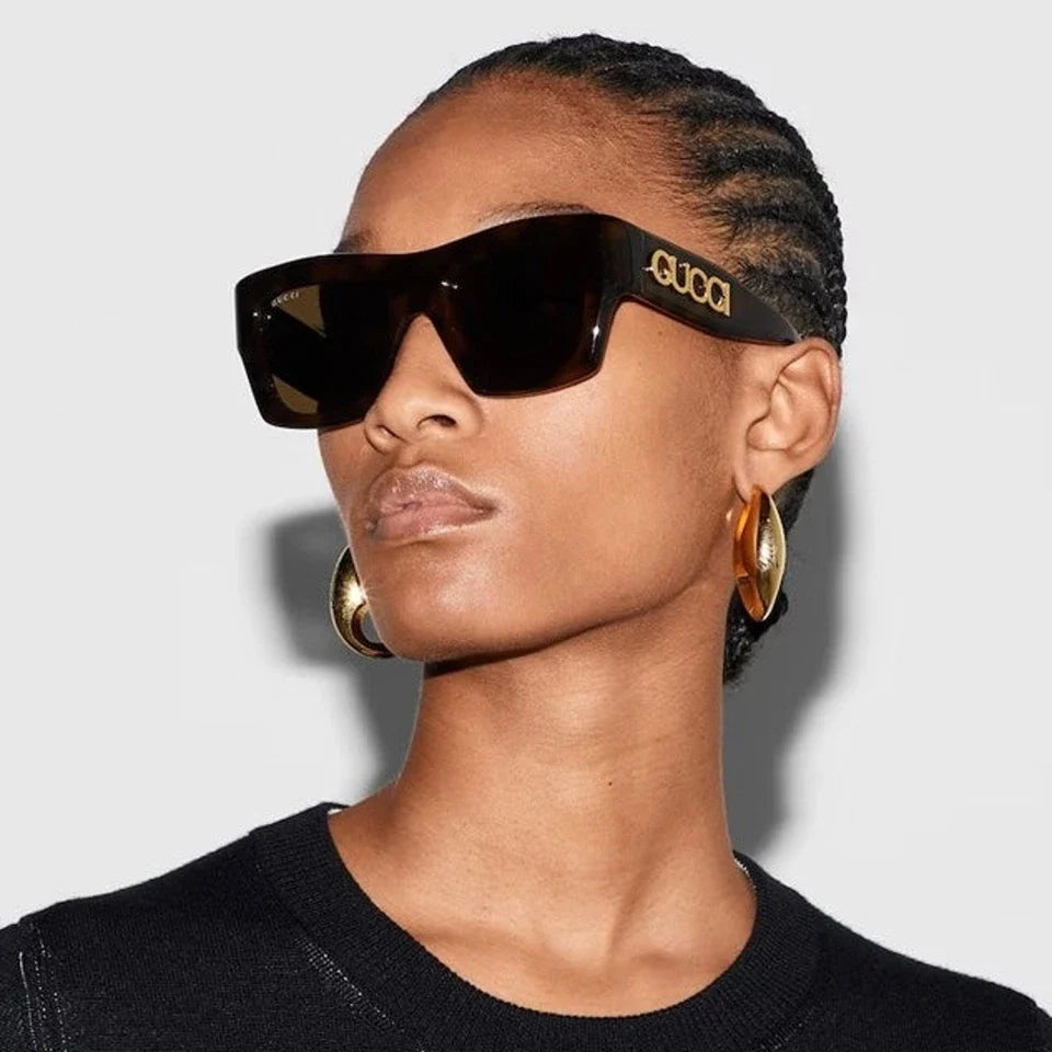 Woman wearing luxury Gucci oversized black sunglasses and gold hoop earrings